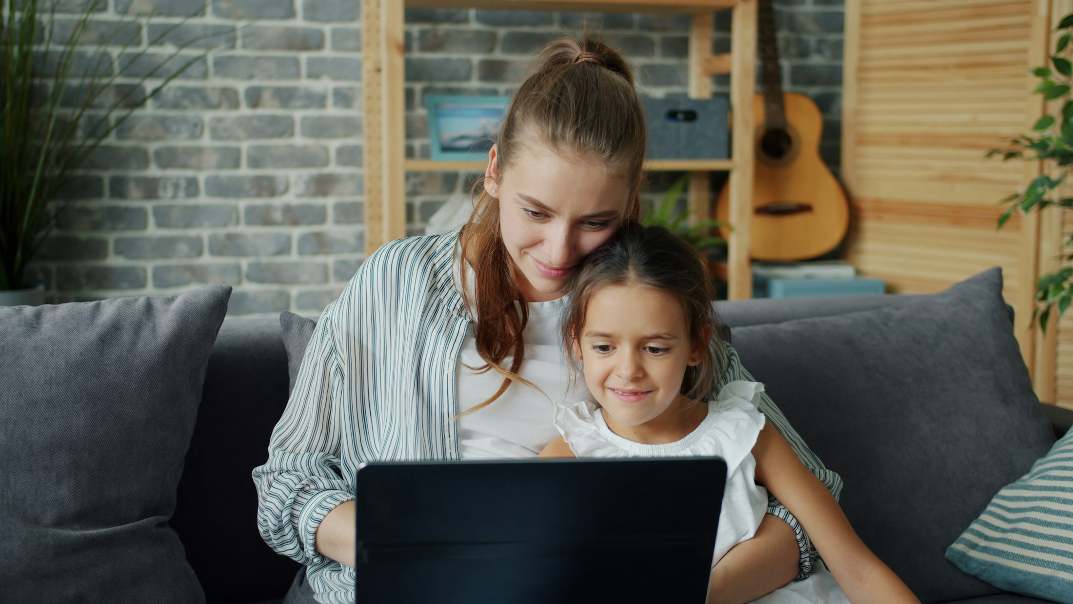 Mãe e filha aproveitando um momento juntas com um notebook no sofá de casa